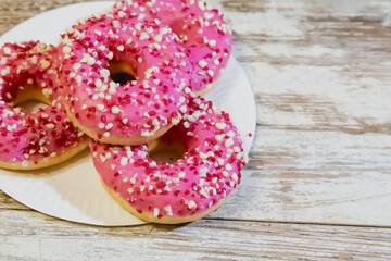 Doughnuts with pink glaze and sprinkles on a white plate on an old kitchen table.