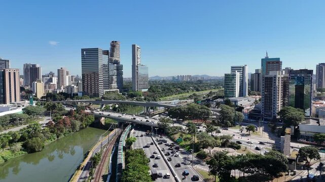 Vis&atilde;o a&eacute;rea revela edif&iacute;cios comerciais modernos alinhados &agrave; Marginal Pinheiros, com tr&aacute;fego intenso e vegeta&ccedil;&atilde;o marginal contrastando com a urbaniza&ccedil;&atilde;o de S&atilde;o Paulo