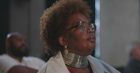 African American woman in the audience with large jewelry, focused and looking up during a religious or spiritual event