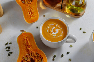 Roasted butternut squash soup with cream and pumpkin seeds on two white mugs.