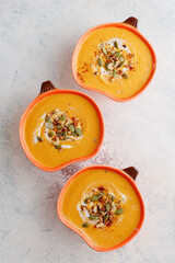 Roasted butternut squash soup with cream and pumpkin seeds on two white mugs.