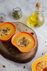Roasted butternut squash soup with cream and pumpkin seeds on two white mugs.