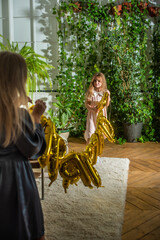 mother and daughter preparing for birthday party. young woman and girl decorating room together. balloon garland