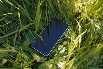 A cell phone with a black screen lies in the grass. A cell phone with the screen turned off against the grass. 