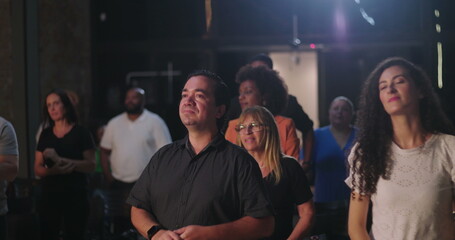 Diverse group of people standing in church during worship, men and women of different ethnicities united in faith, solemn expressions, peaceful moment of prayer and spiritual connection