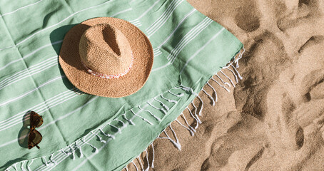 Green towel, straw hat, sunglasses on beach sand background. Aesthetic lifestyle, summer vacation...