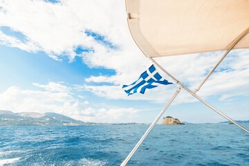Gliding across the sparkling blue waters near Zakynthos, a Greek flag flutters on the boat as sunlight sparkles off gentle waves. The breathtaking landscape invites adventure and exploration