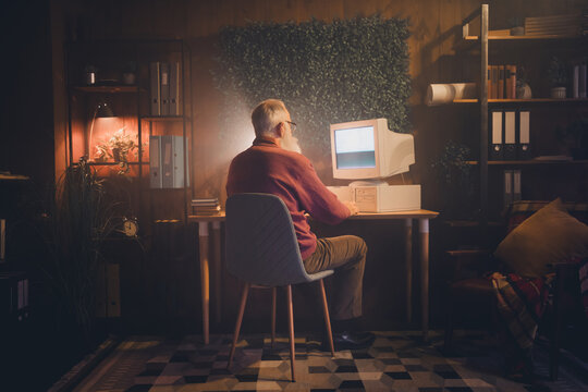 Elderly man working with computer in cozy home office setting during evening