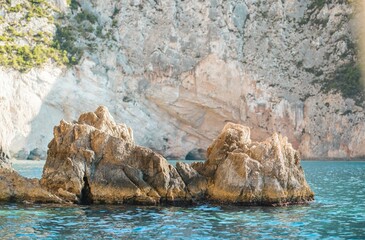 Sparkling turquoise waters gently lap against rugged rock formations in Zakynthos, as summer tourists savor the beauty of this stunning coastal paradise, perfect for adventure and relaxation