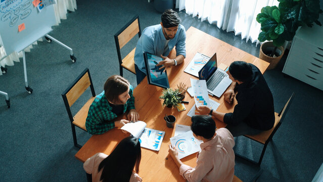 Skilled project manager walking at table while colleague brainstorm idea. Business team working together to plan marketing strategy while looking at data analysis or financial statistic. Convocation.