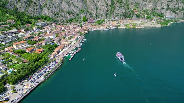 Aerial view of Limone sul Garda, a charming lakeside town with colorful houses, lush lemon terraces, bike paths along Lake Garda, and majestic mountains surrounding the crystal-clear water