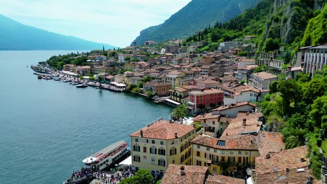 Aerial view of Limone sul Garda, a charming lakeside town with colorful houses, lush lemon terraces, bike paths along Lake Garda, and majestic mountains surrounding the crystal-clear water
