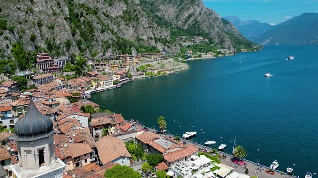 Aerial view of Limone sul Garda, a charming lakeside town with colorful houses, lush lemon terraces, bike paths along Lake Garda, and majestic mountains surrounding the crystal-clear water