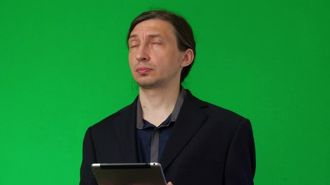 A mid-shot captures the tired and frustrated mood of a man holding a digital tablet, resting his hand on his cheek, against a vibrant green screen, ideal for customizable backdrops