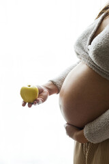 Healthy Pregnancy and getting weight. Pregnant woman holding apple at baby bump in soft window light. Diet and pregnancy
