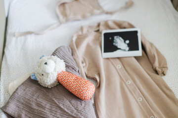 Pregnancy and getting ready for baby. Modern baby crib with stylish baby clothes, toy, boho mobile, ultrasound picture.Preparation and making nursery