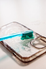 Smartphone case being cleaned with a toothbrush and soap, showcasing a close-up of the cleaning process, highlighting the importance of device maintenance and hygiene practices