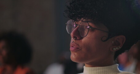 Young person with glasses and nose piercing looking thoughtfully into the distance, side profile, capturing deep focus and reflection in a group setting