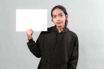 Young Asian man wearing a black hoodie holding a blank white board with a doubtful facial...