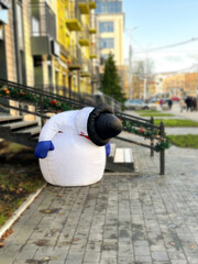 Broken life-sized snowman mascot decorates city center during Christmas season. Image with humor. Broken snowman illustrating poor Christmas and winter without snow.