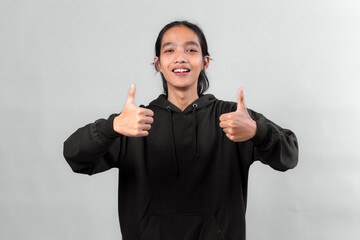 Happy young Asian person in black hoodie smiling while giving two thumbs up, expressing double...
