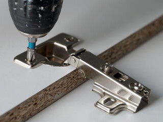 Installing a furniture door hinge, close-up of a power drill screwing in a furniture hinge