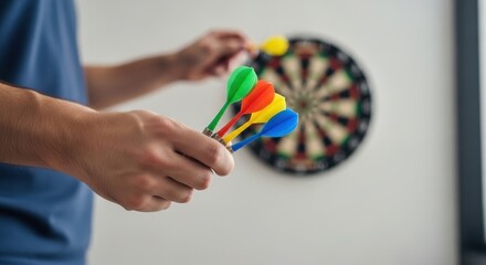 Man holding colorful darts in his hand, preparing to throw at a blurred dartboard in the background. Indoor game.