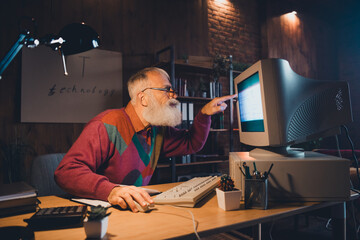 Elderly man in cozy setting using vintage computer indoors during evening reflecting modern...