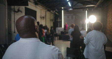 Wide shot of church service with congregation standing and worshipping, back view of people focused...