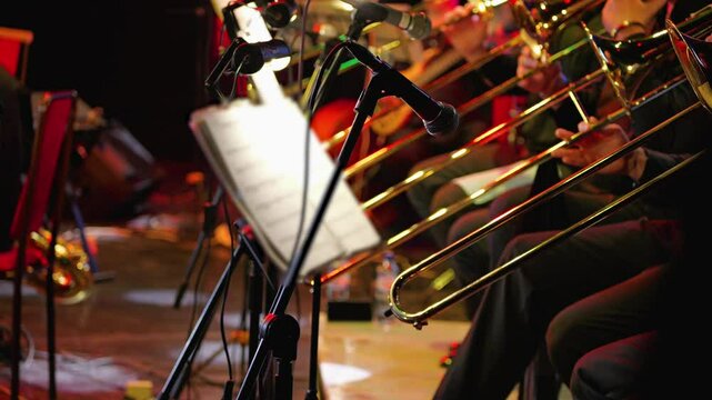 A vibrant orchestral stage with trombones and microphones set up for a live performance. Warm lighting enhances the dynamic atmosphere