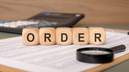 Wooden cubes spelling ORDER on documents with a magnifying glass and calculator