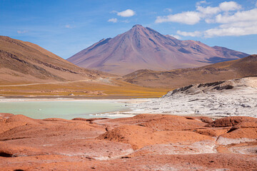 Stunning volcanic landscape in the Atacama Desert, Chile, with vibrant red rocks, salt lake, and mountains under a bright blue sky. High-altitude Andean scenery at its most surreal.