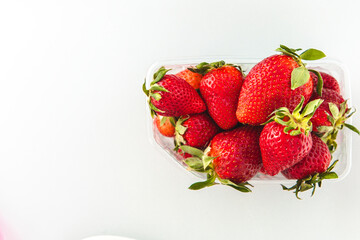 Fresh strawberries in a clear container on a white background during daylight hours