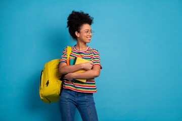 Charming young student with a yellow backpack holding book, wearing a colorful striped T-shirt