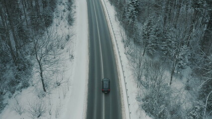 Aerial view of a winding snowy mountain road cutting through a dense winter forest. Mountain road...