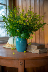 A bouquet of yellow wild flowers in a blue vase on an old wooden window.