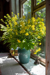 A bouquet of yellow wild flowers in a blue vase on an old wooden window.