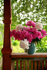 Bouquet of pink and white peonies in a blue vase on an old wooden veranda.