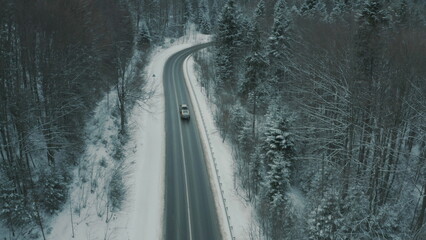 Aerial view of a winding snowy mountain road cutting through a dense winter forest. Mountain road...