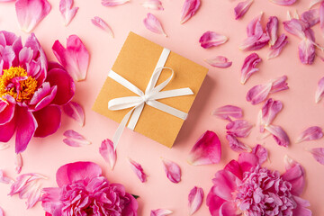 Gift box with white ribbon and pink peony flowers on pastel background with scattered petals