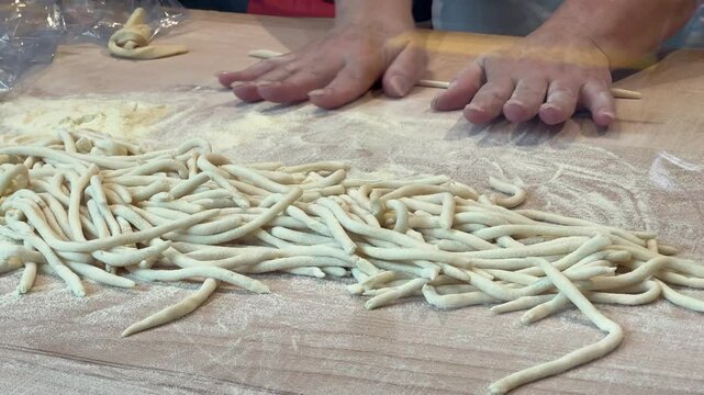 Woman making traditional Italian pici pasta by hand on floured wooden surface
