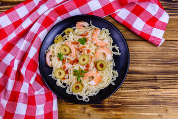 Italian pasta with shrimps and olives in a black plate. Top view