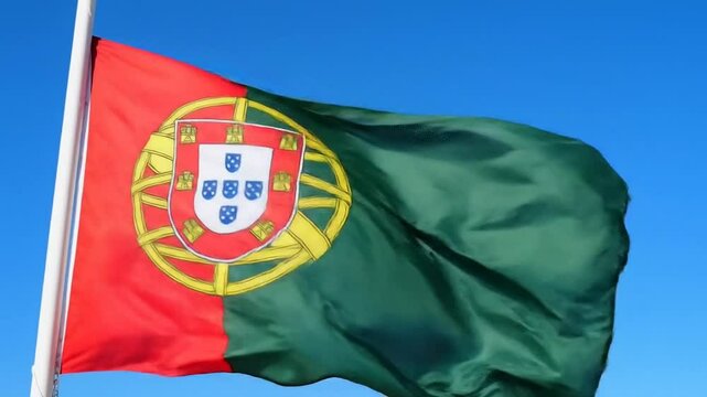 Portugal national flag waving against blue sky background. Detailed view of Portuguese coat of arms and colors. Patriotic image of red and green flag with armillary sphere.