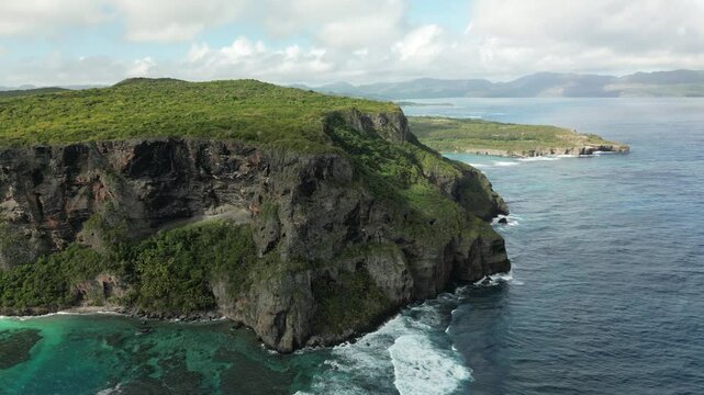 Scenic drone footage of Playa Front&oacute;n, featuring steep cliffs dropping into emerald and turquoise ocean waters under a bright tropical sky