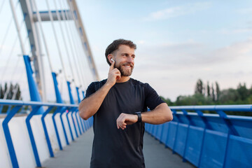Happy young man in earphones enjoy outdoors workout, male jogger listening music and checking...