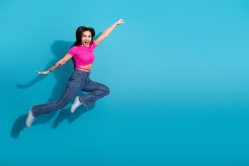 Energetic young woman in casual stylish outfit jumping joyfully against a blue background