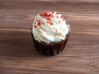 close up of one cupcake with white cream on wooden background