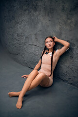 Naklejka premium Young woman with braided hair and butterflies on her shoulder sitting against a textured grey wall in soft lighting