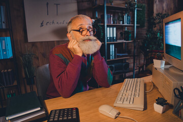 Elderly IT professional working at home office in cozy evening light, using technology and...