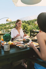 A 20s blonde woman enjoys her breakfast at a hotel table with stunning mountain scenery in the background